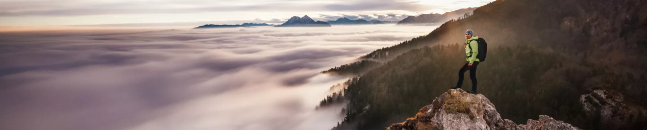 Une femme au sommet d'une montagne avec vue sur la vallée et les nuages.